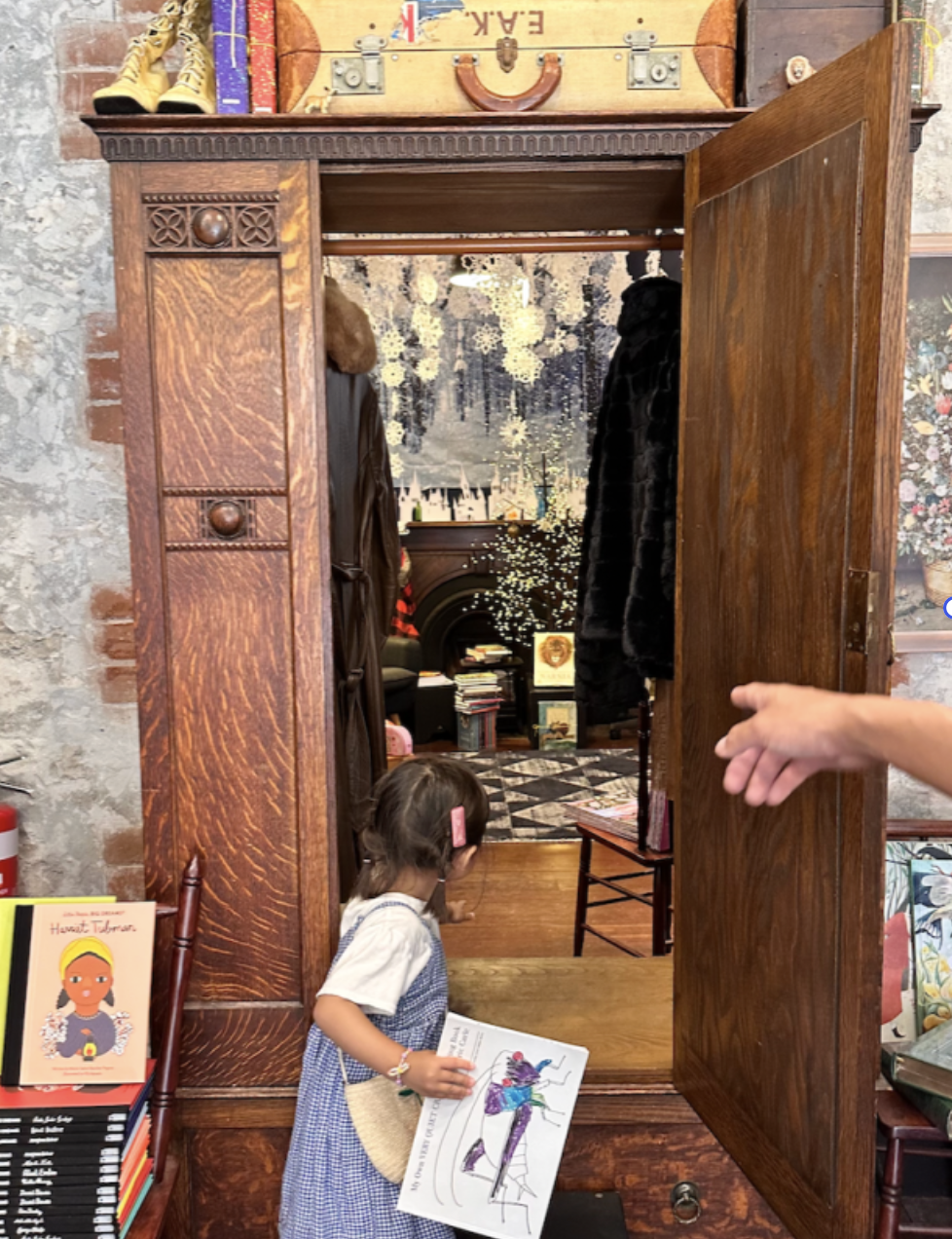 Child entering a wardrobe-style story room holding artwork as part of visual literacy development through worldschooling